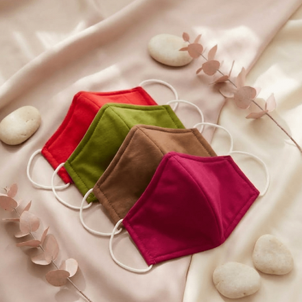 Four colorful face masks on a soft fabric background with stones and leaves.