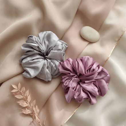 Two scrunchies, one gray and one pink, on a soft fabric background.